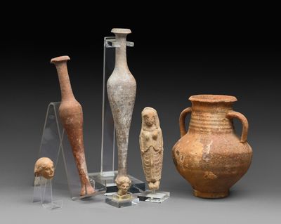 Plusieurs vases anciens et d'autres objets sont exposés sur un socle gris.