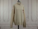 un pull à col roulé beige posé sur un mannequin devant un mur lambrissé de blanc
