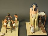 two figurines of pharaohs sitting on a rug next to a statue of a man
