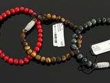 three bracelets of different colors with tags on them on a black surface