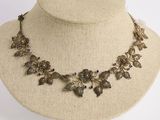 une photo d'un collier porté par un mannequin, orné de fleurs et de feuilles