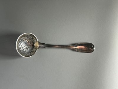 une cuillère en argent et un repose-cuillère posés sur une table, sur fond blanc