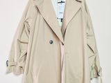 un trench-coat beige suspendu à un cintre devant un mur blanc