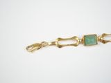 a close up of a gold bracelet with a green stone on it