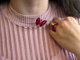 woman wearing a pink sweater and a gold necklace with a red flower on it