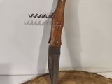 a corkscue with a knife on top of it on a piece of wood