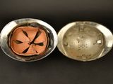 an old silver bowl with a metal lid sitting on a black surface
