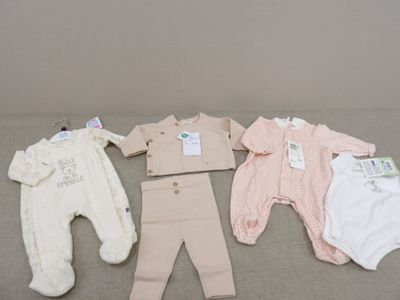 Plusieurs vêtements pour bébé sont disposés sur un lit, avec leurs étiquettes encore attachées.