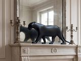 une statue de chat posée sur une cheminée, devant un miroir
