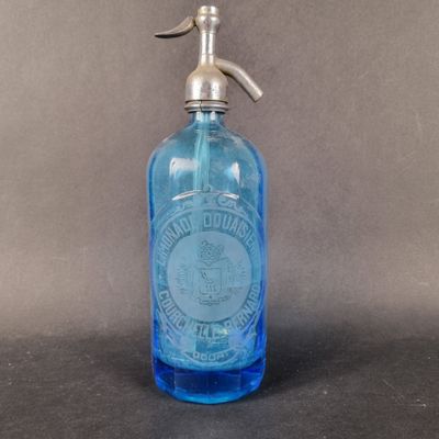 une bouteille en verre bleue munie d'une poignée en métal, posée sur une table