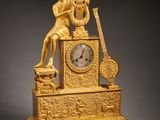 a gold clock with a man playing a musical instrument
