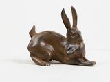 bronze sculpture of a rabbit laying down on a white surface