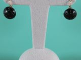 une paire de boucles d'oreilles noires et dorées posées sur un présentoir blanc