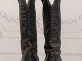 pair of black cowboy boots on a wooden table with a wall in the background