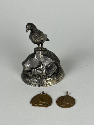 un petit oiseau en métal posé sur un rocher, à côté de deux pièces de monnaie