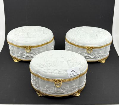 trois boîtes en porcelaine blanche, ornées de bordures et de poignées dorées, posées sur un fond noir