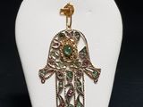 une vitrine blanche sur laquelle est accroché un pendentif en forme de hamsa doré et vert