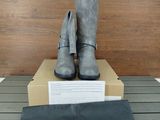 des bottes en cuir gris exposées devant une boîte contenant un sac noir