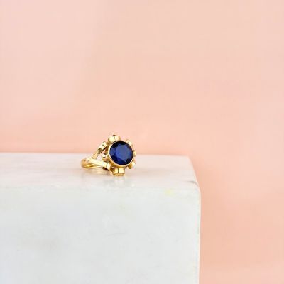 a gold ring with a blue stone sits on top of a marble block