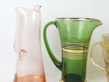 three different colored glass vases on a white surface