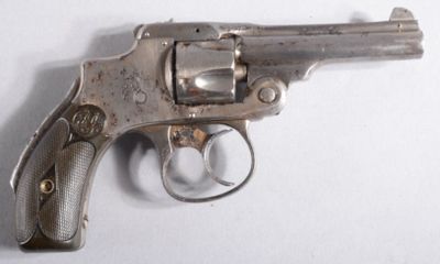 un revolver argenté posé sur une surface blanche, avec un fond blanc