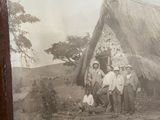 framed photograph of a group of people standing in front of a thatched house