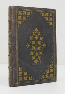 an old book with gold and black cover sitting on a white surface
