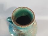a small blue vase with a brown handle on a white surface