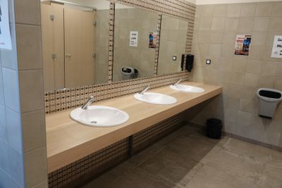 deux lavabos dans des toilettes publiques, avec un distributeur de serviettes en papier fixé au mur
