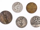 six silver medals of various sizes and shapes on a white surface