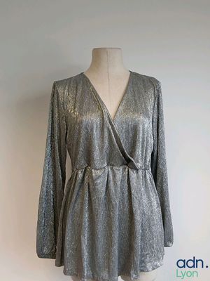 La robe est argentée, elle a des manches longues et un décolleté en V.