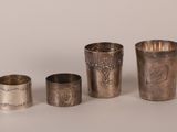 three silver cups and a silver spoon on a white surface