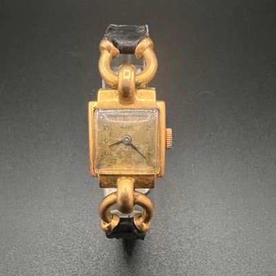 une montre en or, attachée à une chaîne, posée sur un fond noir