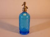 une bouteille en verre bleu avec une poignée en laiton posée sur une surface blanche