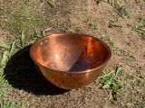 a copper bowl sitting on the ground in the grass