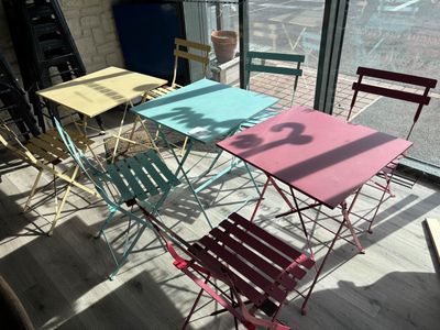 Des chaises et des tables aux couleurs vives sont disposées devant une grande fenêtre