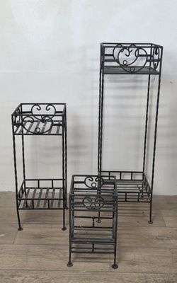 three black metal plant stands sitting on top of a wooden floor