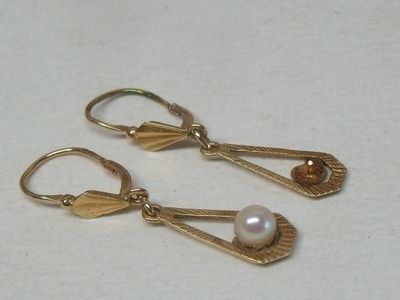 une paire de boucles d'oreilles dorées ornées de perles, posées sur un fond blanc
