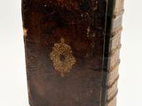 an old brown book sitting on top of a table next to a white wall