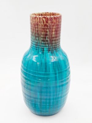 un vase bleu surmonté d'un couvercle rouge, posé sur une surface blanche