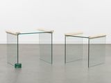 two glass tables in a room with a white wall behind them