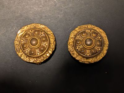 deux boutons dorés posés sur une table, sur fond noir