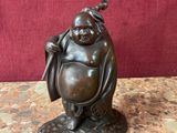 statue en bronze représentant un Bouddha souriant tenant un sac posé sur une table