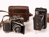 two old cameras sitting next to each other on a white surface