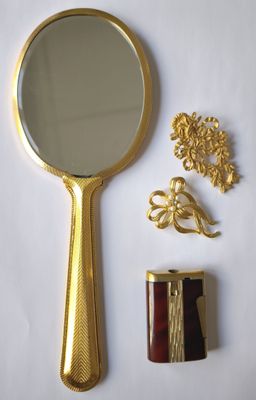 un miroir doré et un ensemble de bijoux en or posés sur une surface blanche