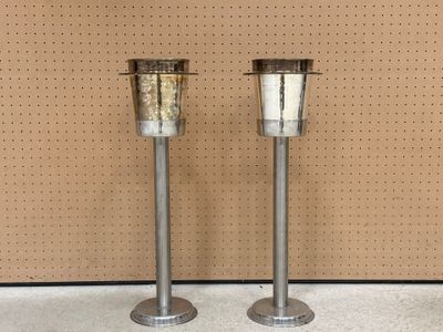 Deux bougies en métal sont posées sur un support devant un mur.