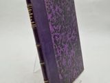 un livre violet aux bords dorés posé sur une surface blanche