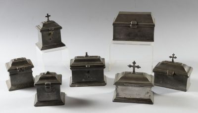 six boîtes en métal argenté, surmontées de croix, posées sur une surface blanche
