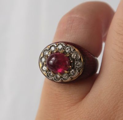une image représentant la main d'une femme tenant une bague sertie d'une pierre rouge
