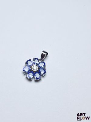 une image représentant un pendentif en forme de fleur bleue et blanche posé sur une surface blanche